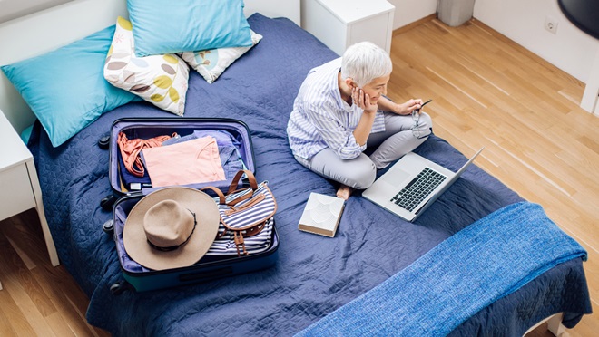 woman sitting on a bed with a suitcase and laptop